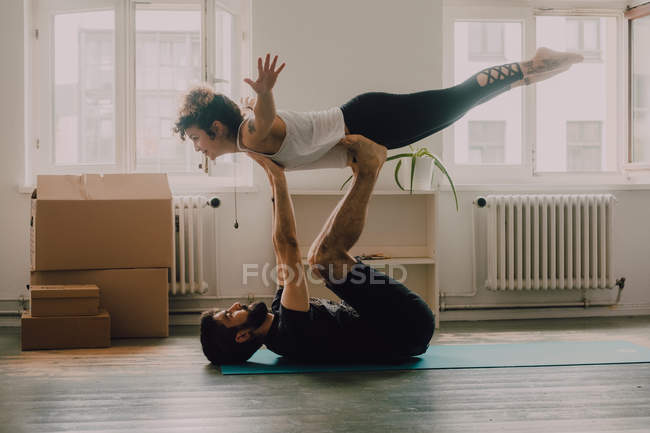 Vista lateral do casal atlético exercitando e equilibrando juntos no chão no apartamento moderno — Fotografia de Stock