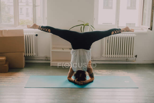Back view of woman in activewear exercising and doing headstand on floor in apartment — Stock Photo