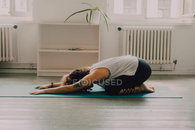 Woman in activewear stretching in child pose on a mat floor at home — Stock Photo