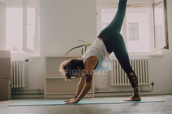 Vue latérale de la femme flexible dans l'exercice de vêtements de sport et debout sur les mains sur le sol dans l'appartement — Photo de stock