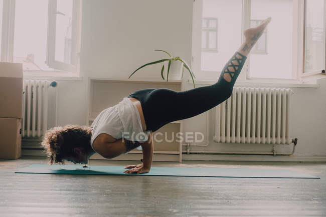 Вид сбоку гибкой женщины в верхней одежде, выполняющей упражнения и стоящей на руках на полу в квартире — стоковое фото