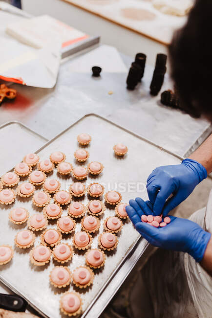Dall'alto pasticceria irriconoscibile che decora la pasticceria rosa su vassoio mentre lavora in pasticceria — Foto stock