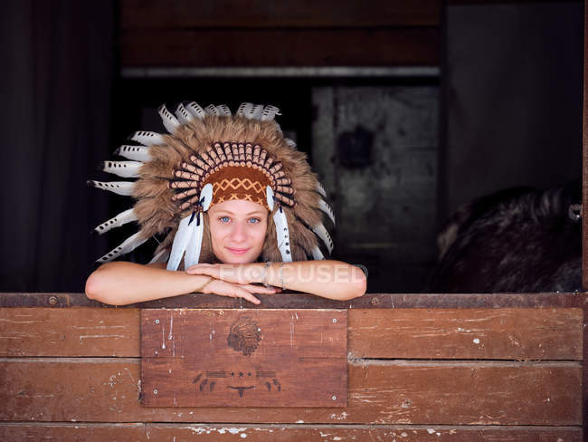 Восхитительная женщина в традиционном индийском перо войны шляпа опираясь на деревянный забор на ранчо — стоковое фото
