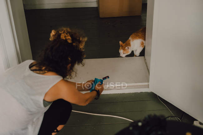 Зверху випадкова жінка дає їжу допитливій кішці, сидячи на підлозі в квартирі — стокове фото