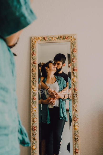 Reflection of tender kissing couple in tall decorated mirror — Stock Photo