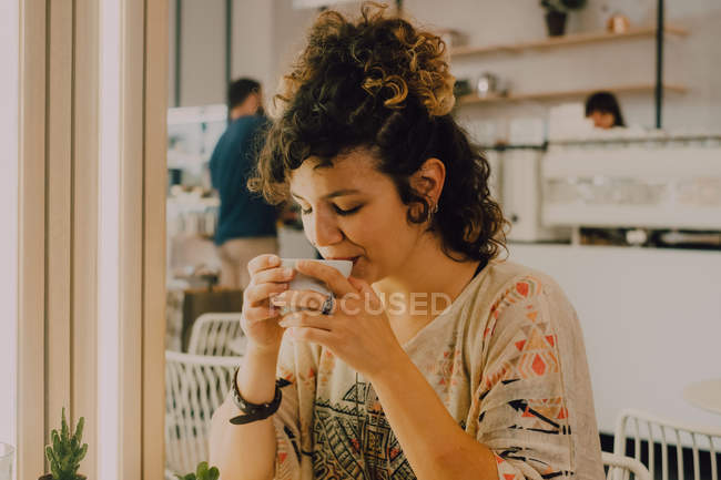 Side view of happy smiling woman sipping from mug while sitting in modern coffee shop — Stock Photo