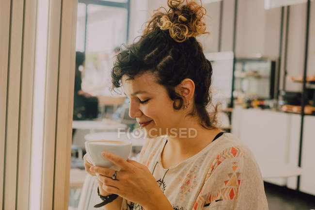Вид сбоку счастливой улыбающейся женщины, пахнущей кружкой, сидя в современной кофейне — стоковое фото