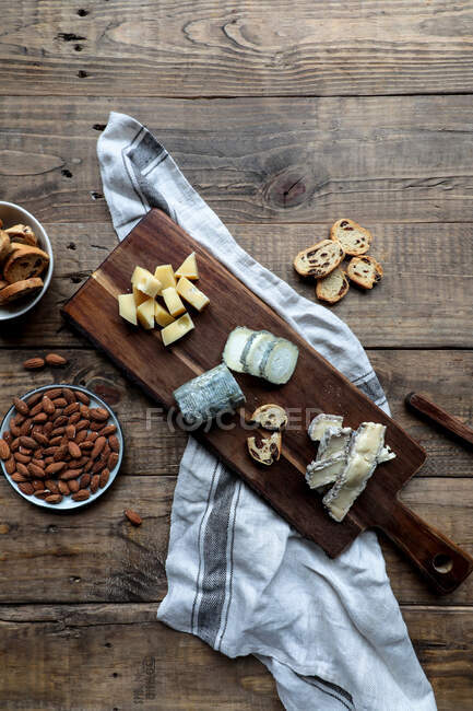 Croutons doces com passas e prato com amêndoas colocadas em mesa de madeira perto da placa com vários queijos cortados — Fotografia de Stock