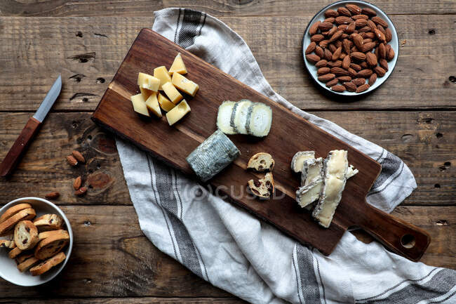 Солодкі грінки з родзинками і тарілкою з мигдалем розміщені на дерев'яному столі біля дошки з різними нарізаними сирами — стокове фото