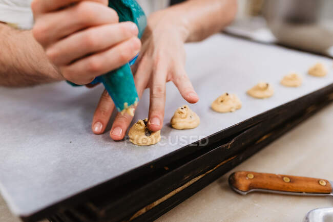 Anonyme Köchin drückt frischen Teig auf Blech mit Papier, während sie an verschwommenem Hintergrund der Bäckerei arbeitet — Stockfoto