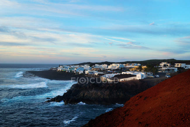 Increíble paisaje de casas blancas situadas en la remota costa del tranquilo mar azul bajo un cielo infinito en Lanzarote, Islas Canarias, España - foto de stock