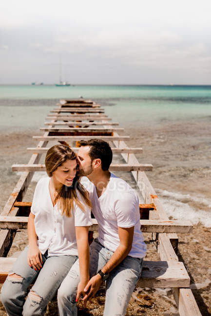 Glad lovers sitting on destroyed pier on seashore — Stock Photo