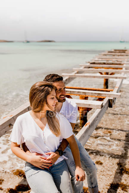 Glad lovers sitting on destroyed pier on seashore — Stock Photo