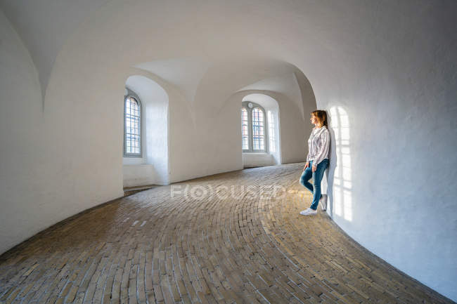 Casual woman leaning on wall in spacious gallery with windows — Stock Photo