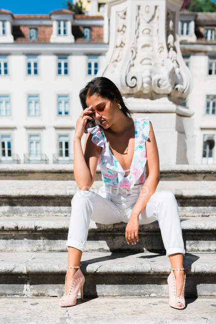 Belle femme détendue en tenue tendance assise sur un escalier en pierre dans une rue pittoresque — Photo de stock