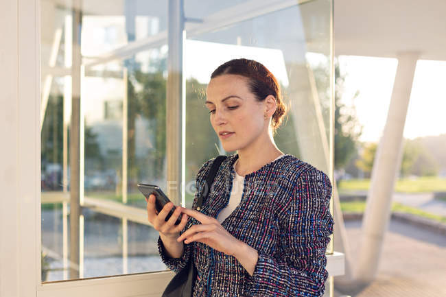 Cheerful female entrepreneur smiling and looking away while talking on smartphone and standing on street — Stock Photo