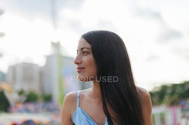 Mulher calma Wistful com cabelos longos em sundress de pé ao lado da atração no parque de diversões no dia ventoso de verão — Fotografia de Stock
