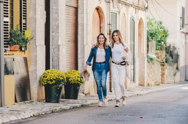 Молоді привабливі усміхнені жінки ходять і насолоджуються зібранням, обіймаючись на прекрасній вулиці з прикрашеними квітами. — стокове фото