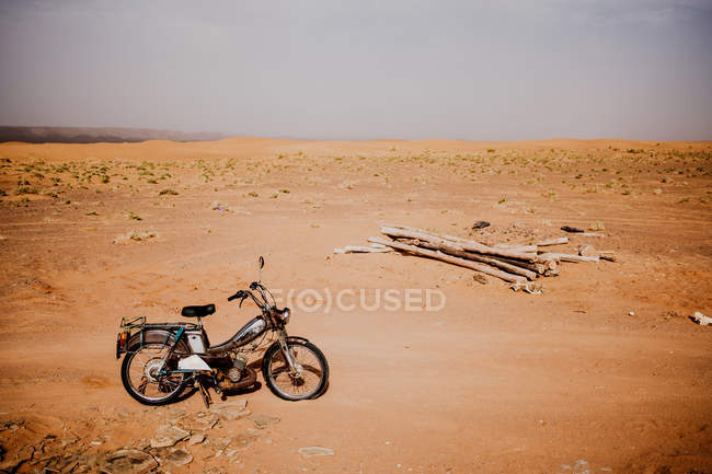 Moto parcheggiata vicino mucchio di tronchi nel deserto arido in Marocco — Foto stock