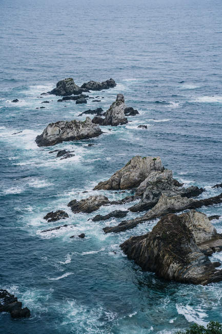Сверху каменистые серые вершины, омываемые пенной голубой водой в открытом море — стоковое фото