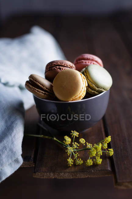 Yellow dill flowers placed on wooden table near bowl of fresh colorful macaroons — Stock Photo
