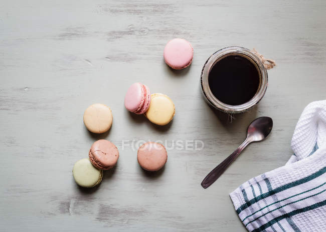 Top view of dessert spoon and cotton towel placed near cup of fresh coffee and colorful macaroons on white table — Stock Photo