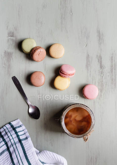 Вид сверху на ложку десерта и хлопок, расставленные рядом с чашкой свежего кофе и разноцветными макаронами на белом столе — стоковое фото