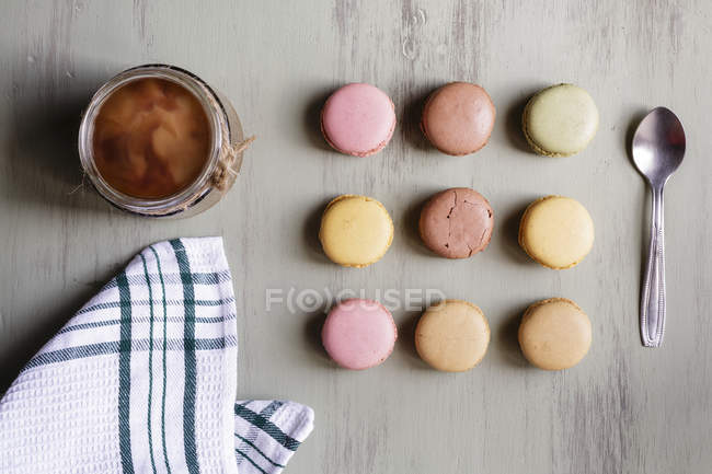 Vista dall'alto del cucchiaio da dessert e dell'asciugamano di cotone posizionati vicino alla tazza di caffè fresco e macaron colorati sul tavolo bianco — Foto stock