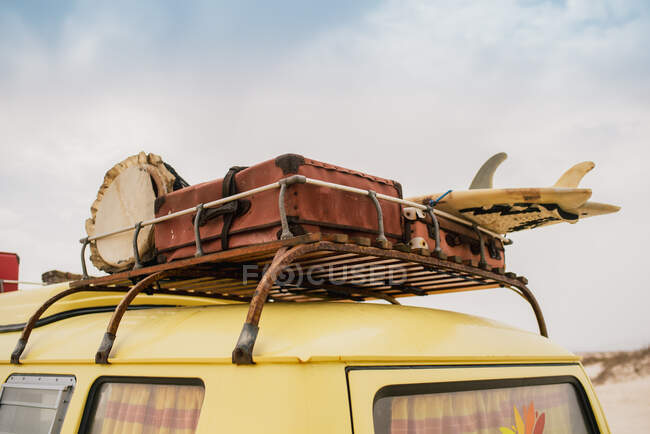 Іржава багажна стійка жовтого автомобіля, завантажена старовинними валізами та серфінгом — стокове фото