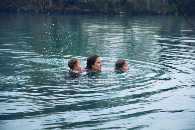 Серед дорослої жінки з маленькими дітьми, які плавають у теплому ставку, проводячи час на відкритому морі. — стокове фото