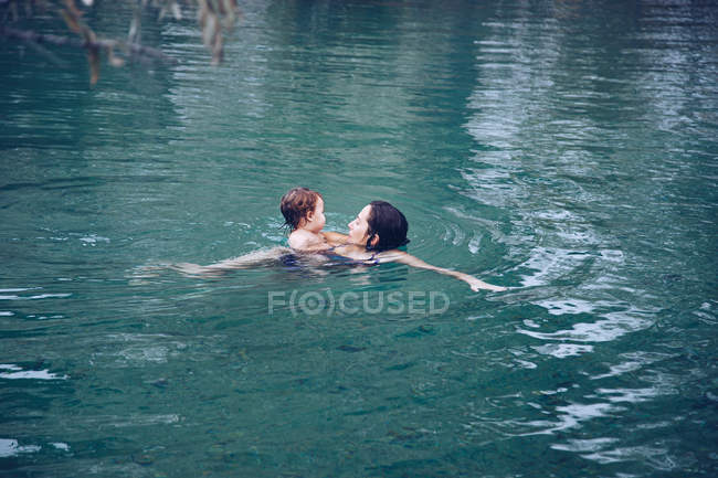 Femme adulte avec petite fille nageant dans l'eau chaude de l'étang tout en passant du temps dans un spa extérieur — Photo de stock