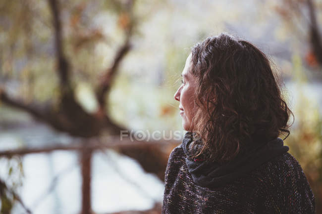 Mujer con el pelo rizado mirando hacia otro lado en el fondo borroso del tranquilo parque de otoño - foto de stock