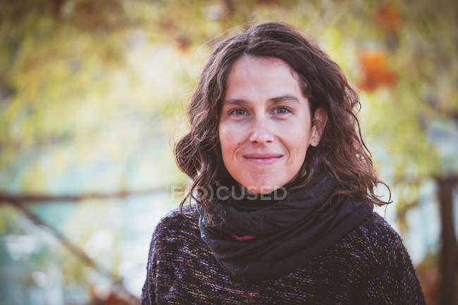 Senhora adulta média com cabelo encaracolado olhando na câmera no fundo borrado do parque de outono pacífico — Fotografia de Stock