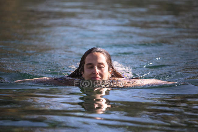 Adult female with closed eyes swimming in clean warm water of pond in spa and enjoying sunny daytime — Stock Photo