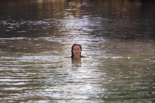 Mulher adulta olhando na câmera enquanto nada em água morna limpa da lagoa no spa e desfrutando de sol durante o dia — Fotografia de Stock