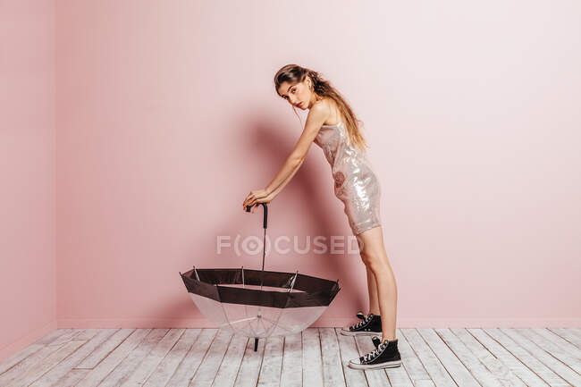 Вид спереди молодой девушки, позирующей с зонтиком на розовом фоне — стоковое фото