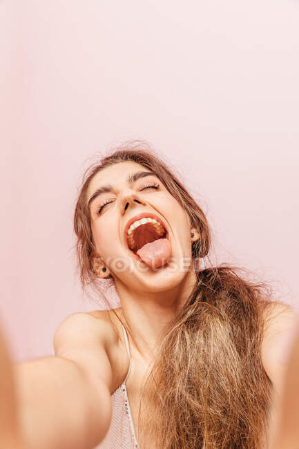 Retrato de una adolescente haciendo una selfie con expresión de felicidad sobre fondo rosa - foto de stock