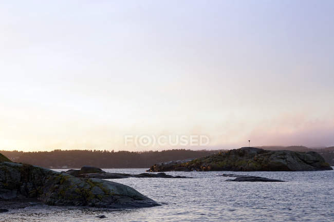 Grey rocks at peaceful seaside on chilly misty day with light colourful sky — Stock Photo
