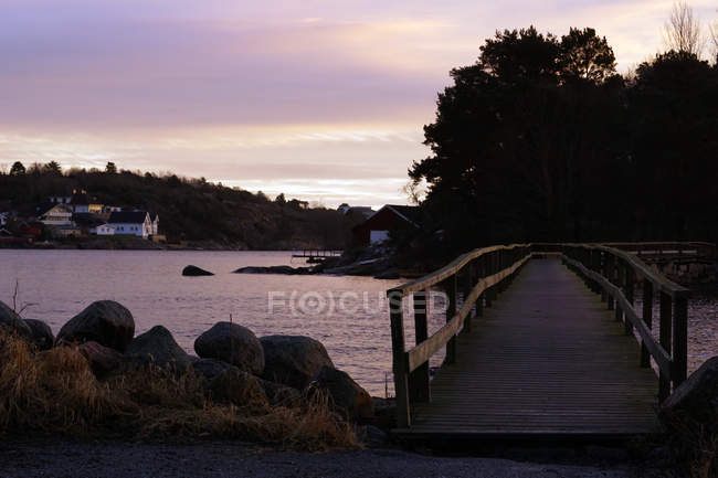 Puente de madera y edificios coloridos a orillas y cielo nublado pastel reflejando en la superficie aún de agua. - foto de stock