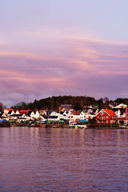 Edificios coloridos en la orilla y cielo nublado pastel que reflejan en la superficie aún de agua. - foto de stock