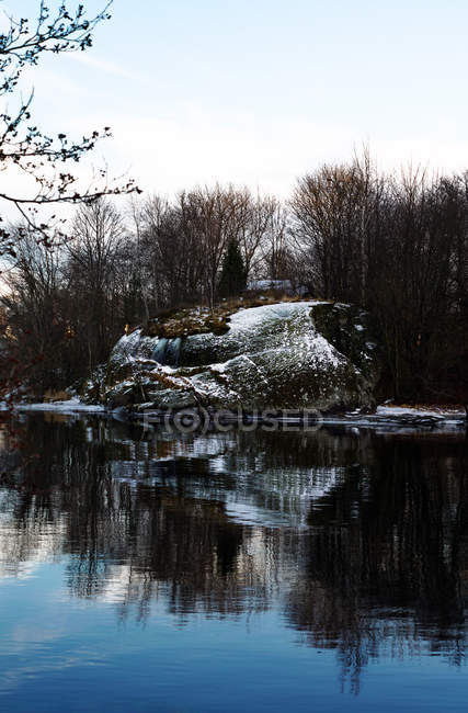 Lato fiume ricoperto di neve e alberi senza foglie che riflettono in acqua morta — Foto stock