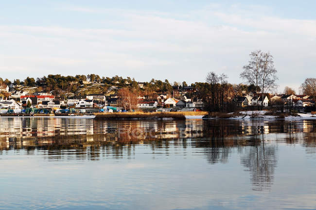 Margem do rio de inverno com árvores sem folhas e casas coloridas à distância — Fotografia de Stock