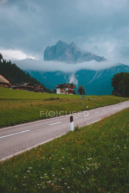 Highway beside cottage village on hill near green dense forest against beautiful mist mountains in Dolomites during summer overcast weather — Stock Photo