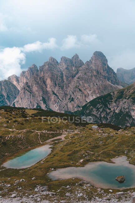 Два озера с чистой голубой водой на зеленых скалистых холмах на фоне серых гор в Доломитовых Альпах в ясную погоду — стоковое фото