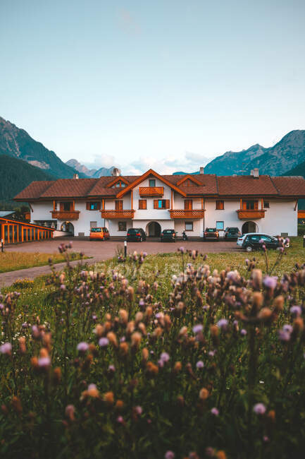 Grand bâtiment blanc et brun sur prairie avec herbe verte épaisse contre de belles montagnes brumeuses dans les Dolomites par temps couvert — Photo de stock