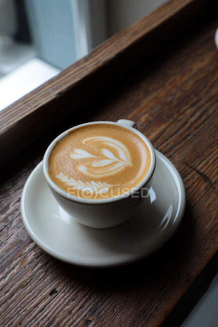 Сверху на деревянном столе в кафе подается чашка свежего капучино с формой сердца на пене — стоковое фото