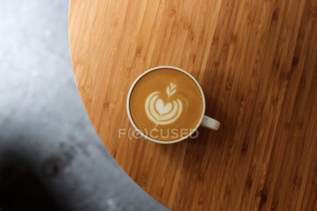 Von oben Tasse frischen Cappuccino mit Herzform auf Schaum serviert auf Holztisch im Café — Stockfoto