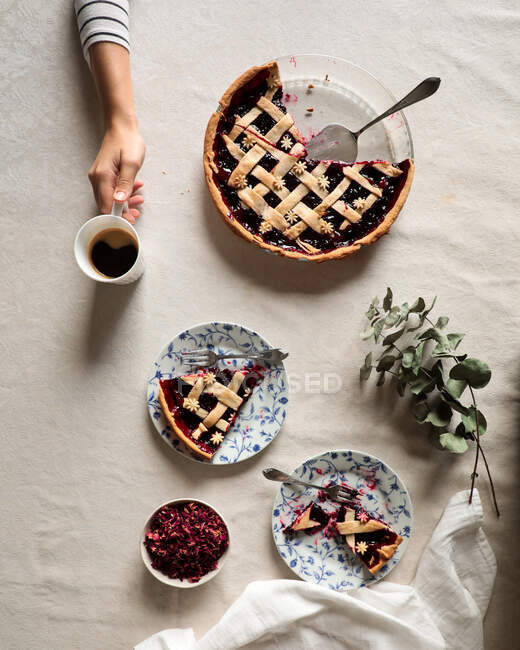 De cima pessoa de colheita sentado à mesa coberta com café servido e deliciosa torta de baga assada no fundo branco — Fotografia de Stock