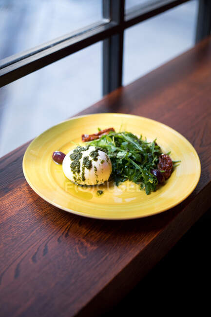 Von oben servierte Mahlzeit mit leckerem pochiertem Ei mit Pesto-Sauce und frischem Grün auf Holztisch am Fenster im Café — Stockfoto