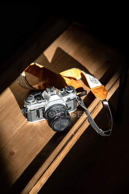 From above retro photo camera with leather belt on wooden table against black background — Stock Photo